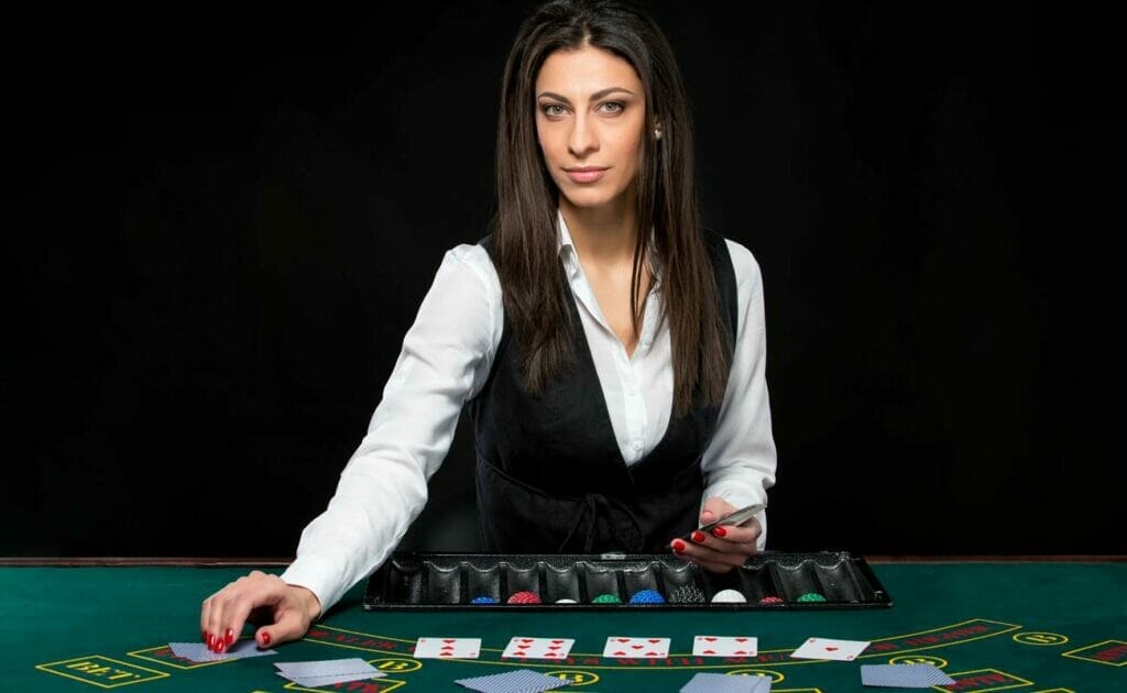 A dealer places cards on the felt with a casino chip tray in front of her.