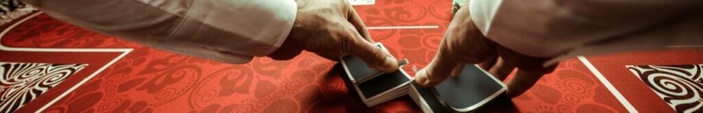 A dealer shuffling playing cards on a red table.