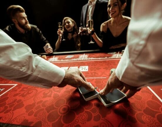A dealer shuffling playing cards on a red table.