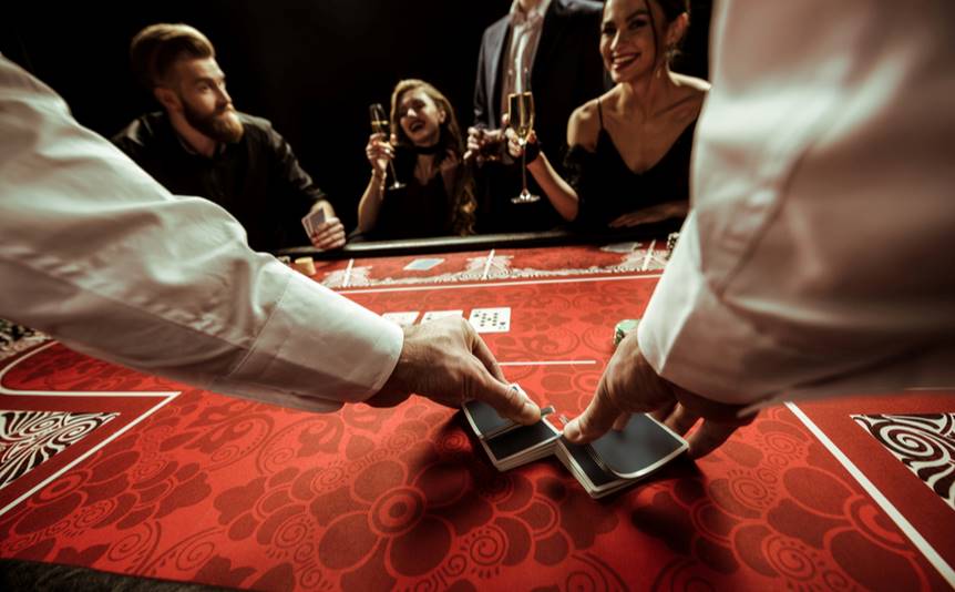 A dealer shuffling playing cards on a red table.