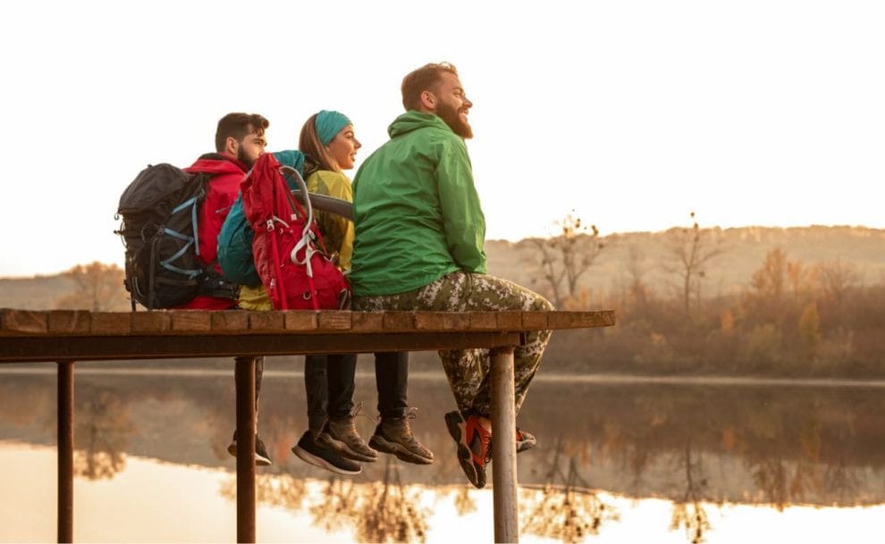  Three hikers sitting on a wooden dock looking out over a lake at sunset.