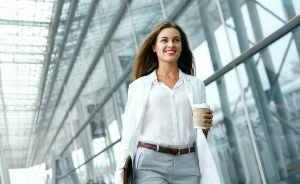 A woman wearing a blazer with a button-up shirt and suit pants with a coffee in her hand.