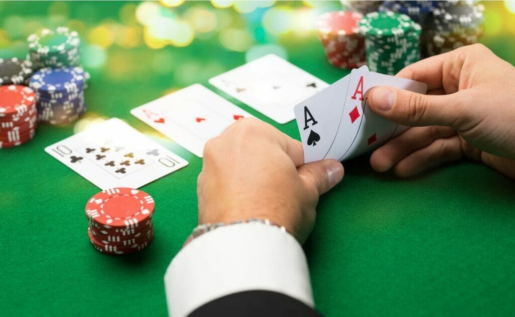 A man sitting at a poker table looking at two aces in his hand.