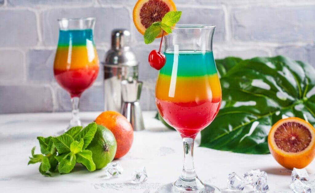 A glass layered with a rainbow mocktail with cherry and orange.