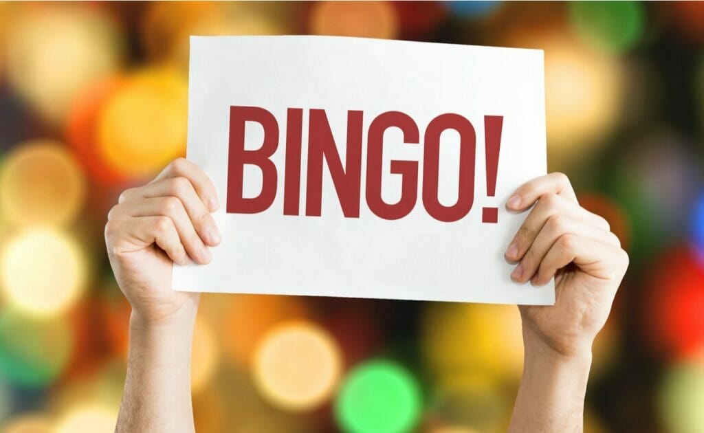 Someone holds a sign up saying “bingo” with lights in the background.