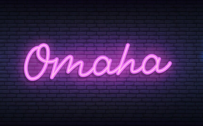 The word ‘Omaha’ lit up in purple neon lights on a brick wall.