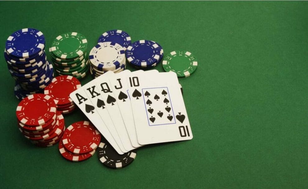 A poker hand showing a royal flush in spades, with poker chip stacks on a green table.