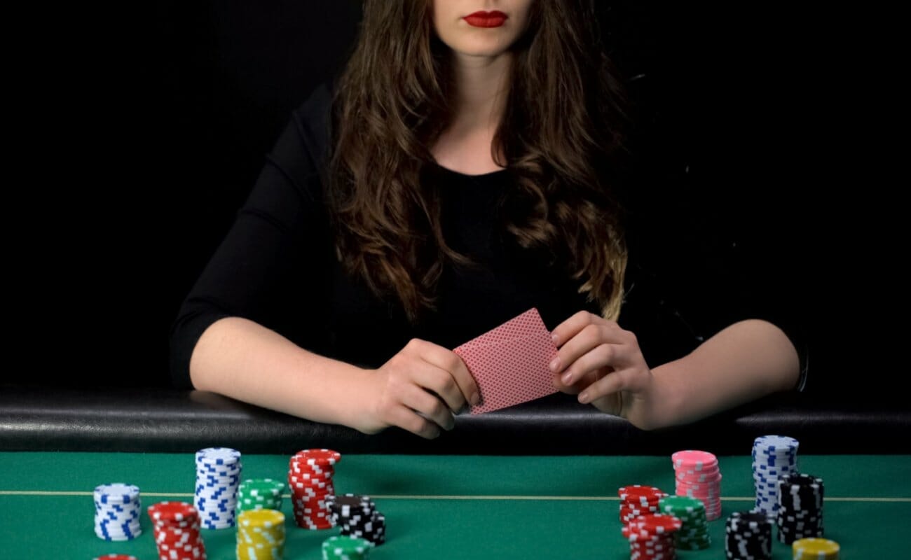  A woman playing poker at a green felt table with casino chips and playing cards.