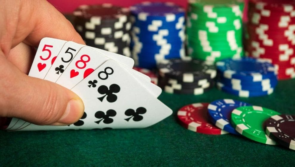 An Omaha player checks their hole cards – two pairs of fives and two eights – behind several stacks of poker chips.