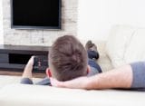 A man relaxes on the couch with a remote in his hand.