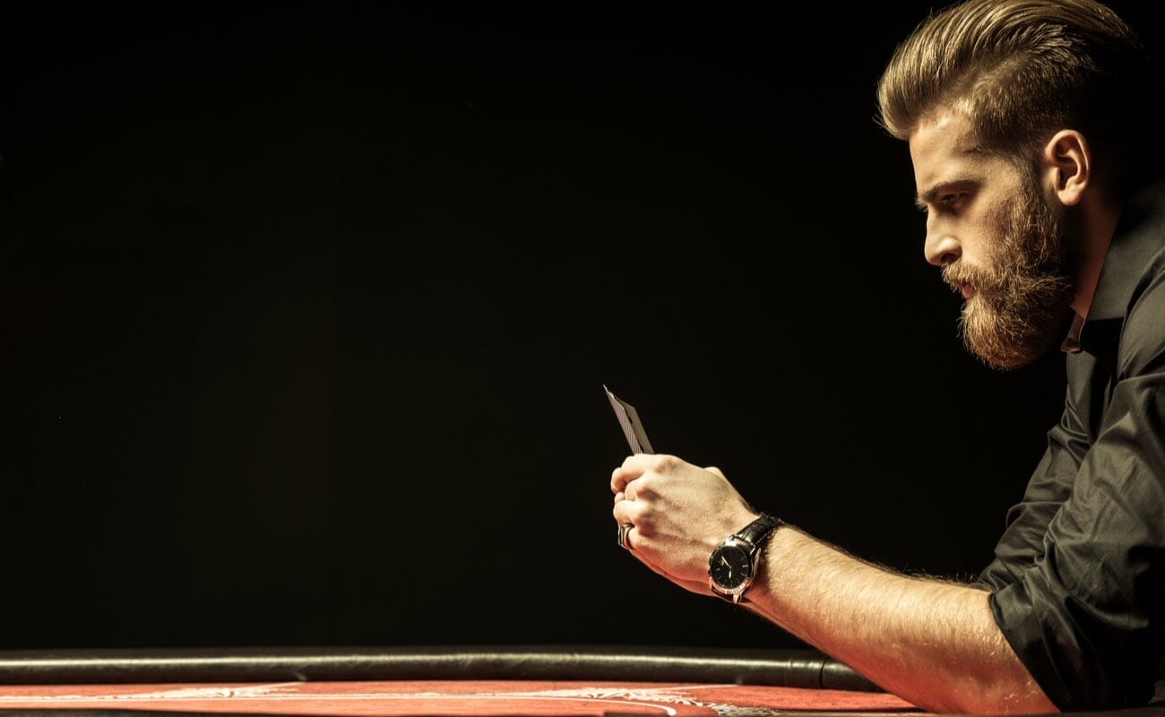 A man sitting at a casino table looking at poker cards.