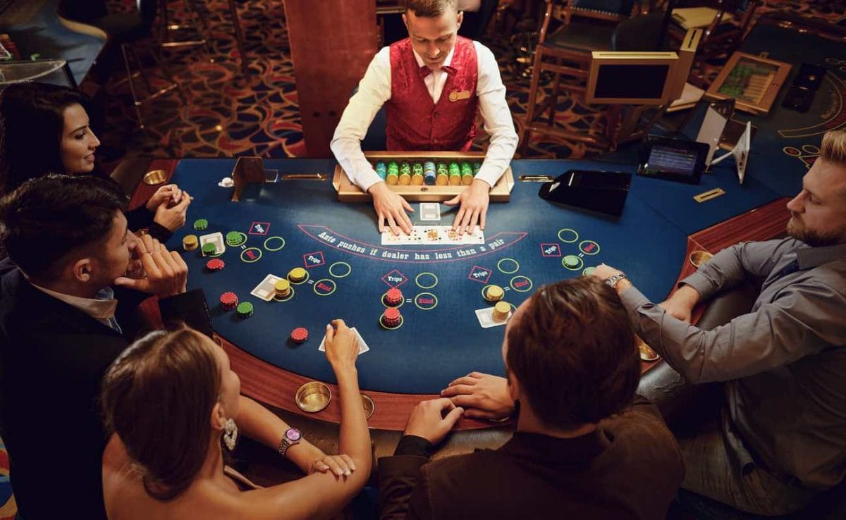 A group of people playing poker with a croupier revealing the community cards.