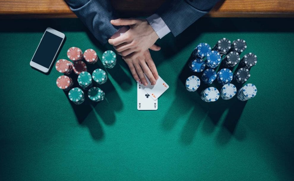 A poker player reveals his hole cards which are a pair of aces. His cards are surrounded by stacks of poker chips on either side.