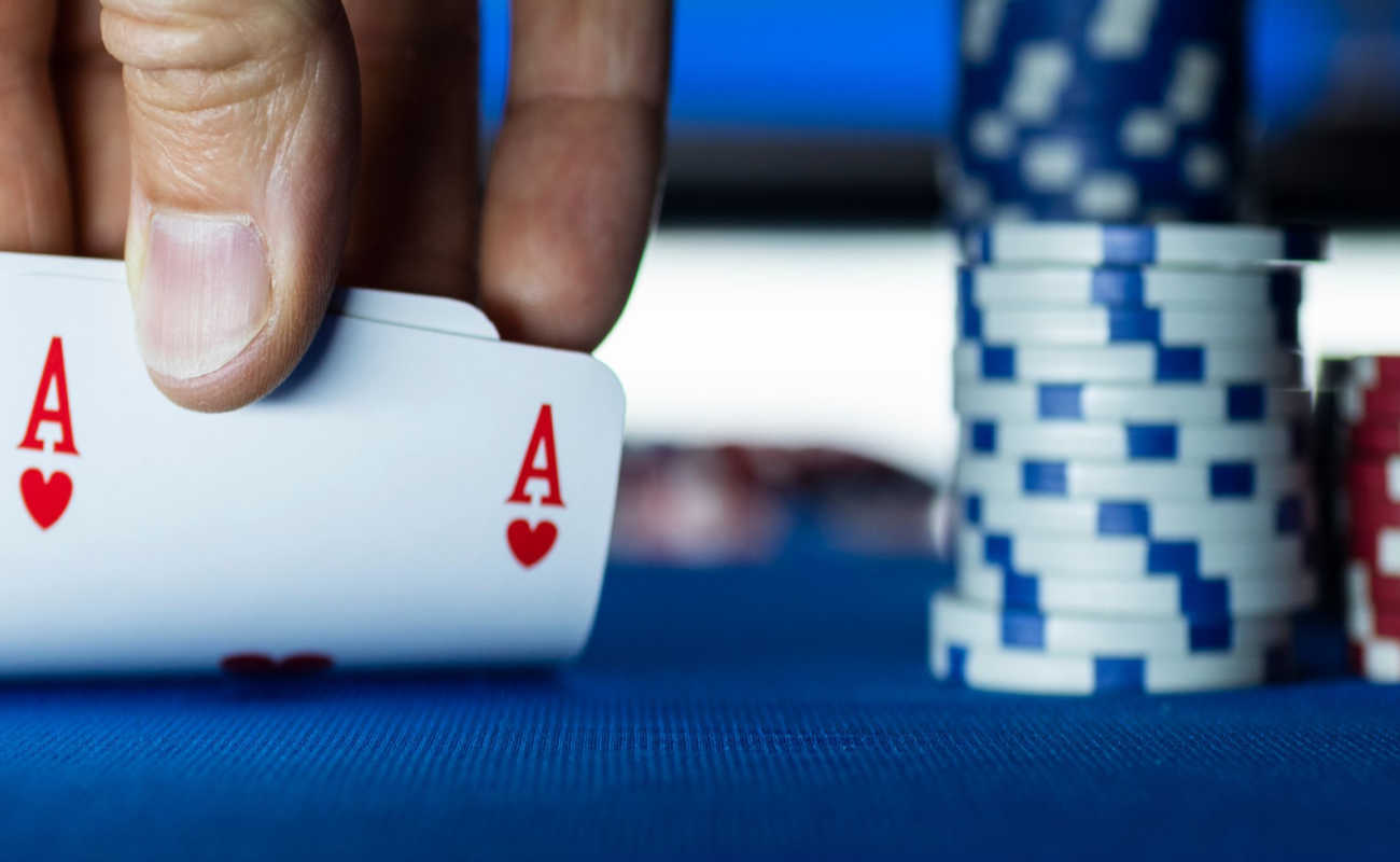 A person holds up two aces next to a stack of chips