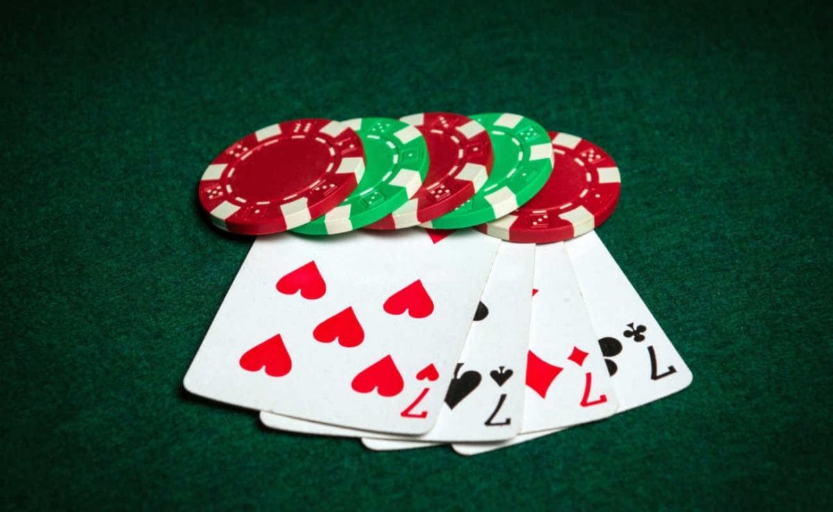 A hand of four 7s next to some poker chips.