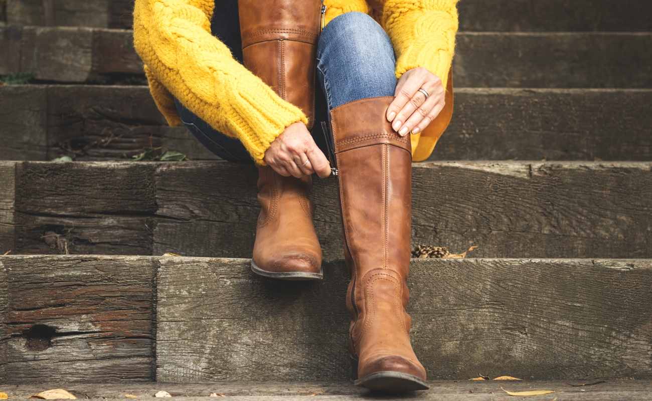 A woman sitting on steps zips up her boots.