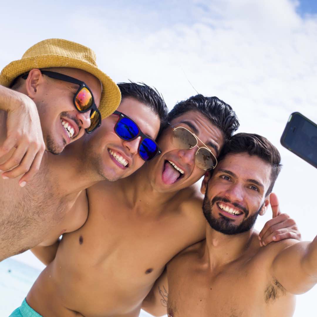 Four men take a selfie at the beach.