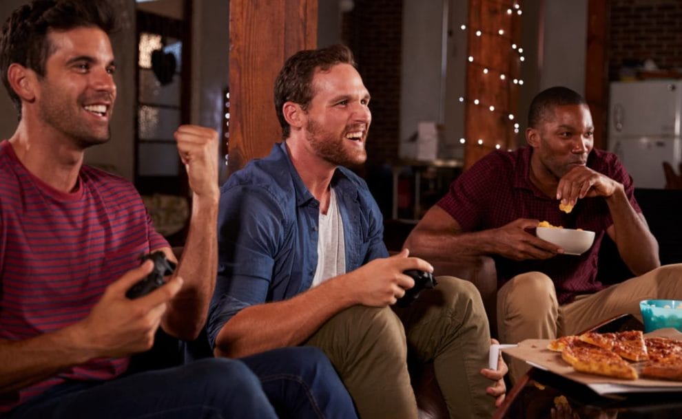 Three guys eating pizza and playing PlayStation.