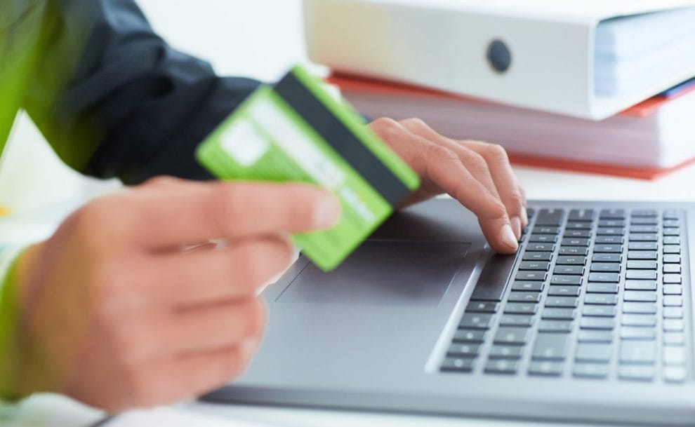 A businessman holding a credit card and typing on a laptop.