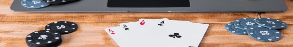 Poker cards and chips on a wooden table with a laptop.