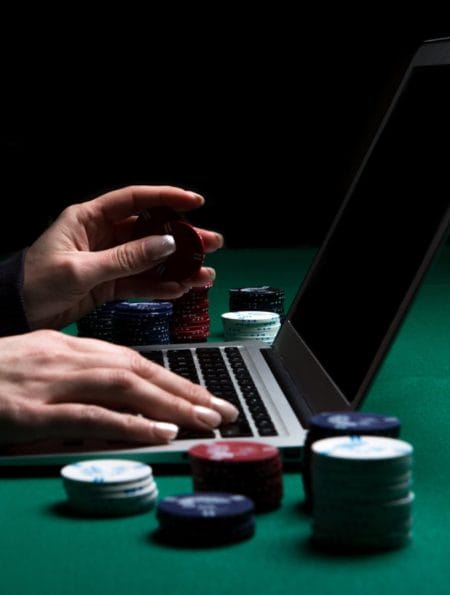 A person playing on a laptop with some poker chips next to him.