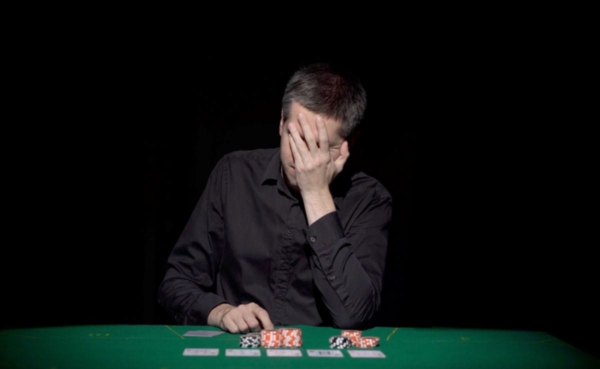 A man holds his hand to his face at the poker table.