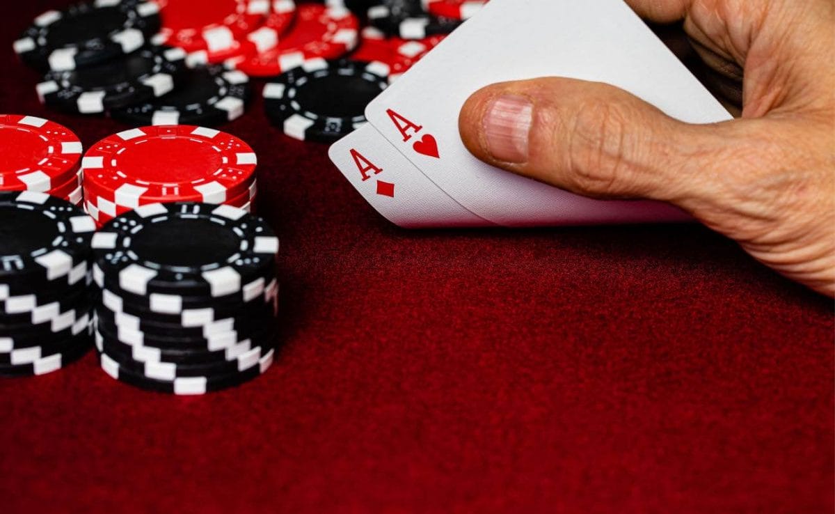 A hand showing two aces on a red felt table with red and black betting chips.