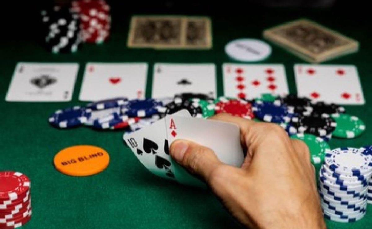 A hand showing an ace in the hole for four aces in Texas Hold-em, on a green felt table with betting chips.