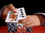 A poker player shows a 10 and a jack in his hand with poker chips in front of him.