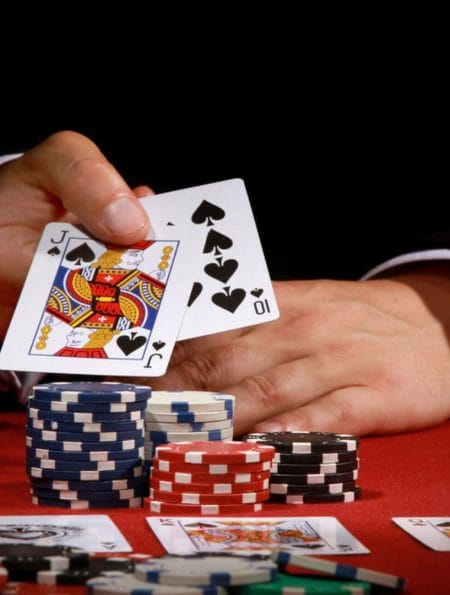 A poker player shows a 10 and a jack in his hand with poker chips in front of him.