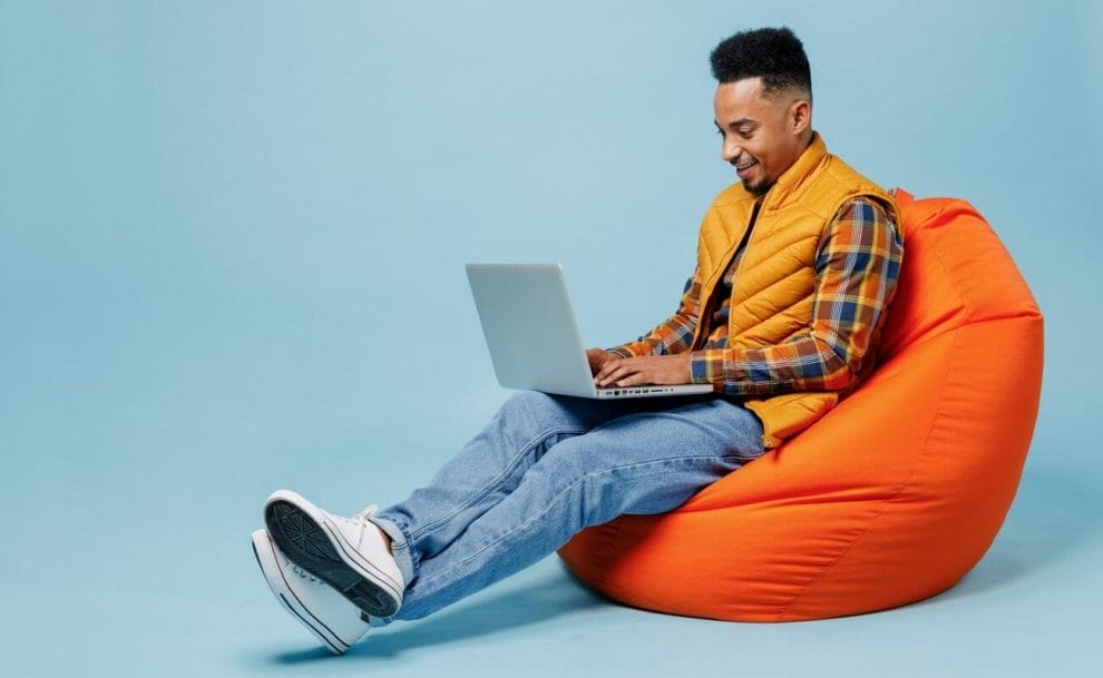 A man sitting on a beanbag using a laptop.