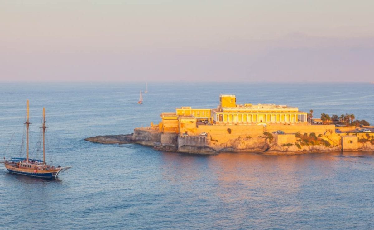 A boat entering St George's Bay in St Julian in Malta, with a casino in the background.