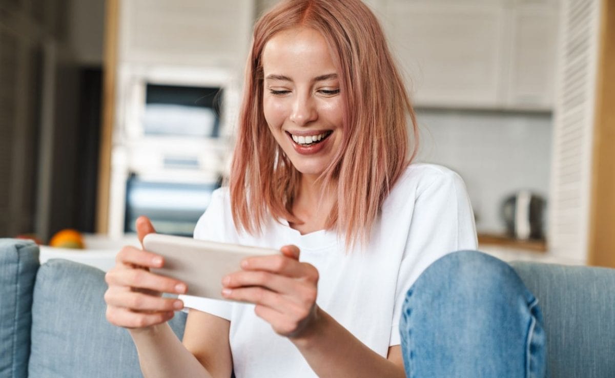 A woman smiling while sitting on a couch using her smartphone.