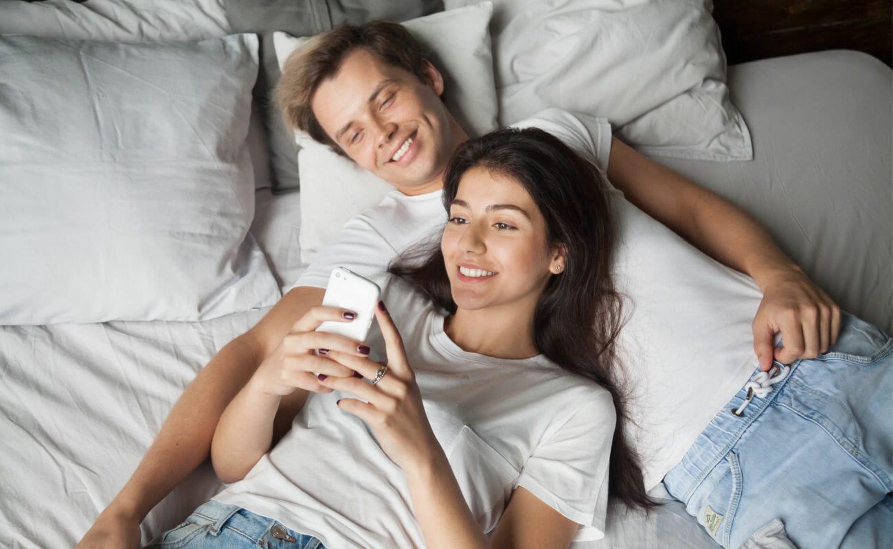 A couple lying in bed looking at a smartphone.