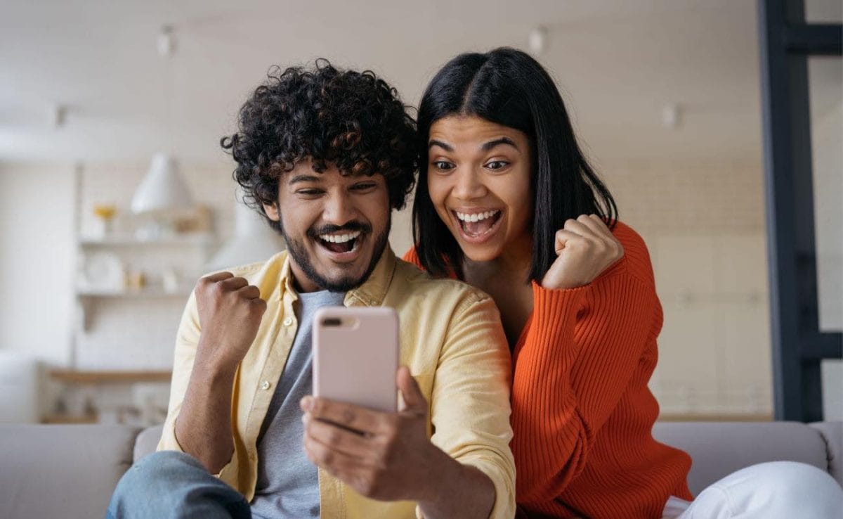 An excited couple cheering as they celebrate a win on a smartphone.