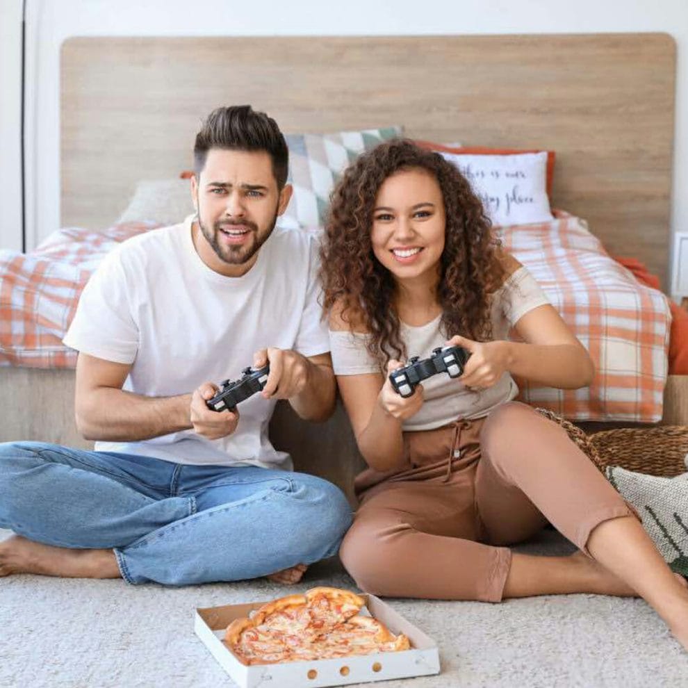 A couple playing video games on the floor of their bedroom.