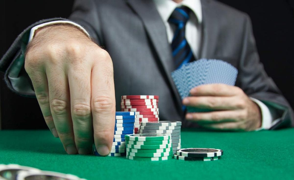 A poker player picks up a stack of chips at the table while holding his cards in his other hand.