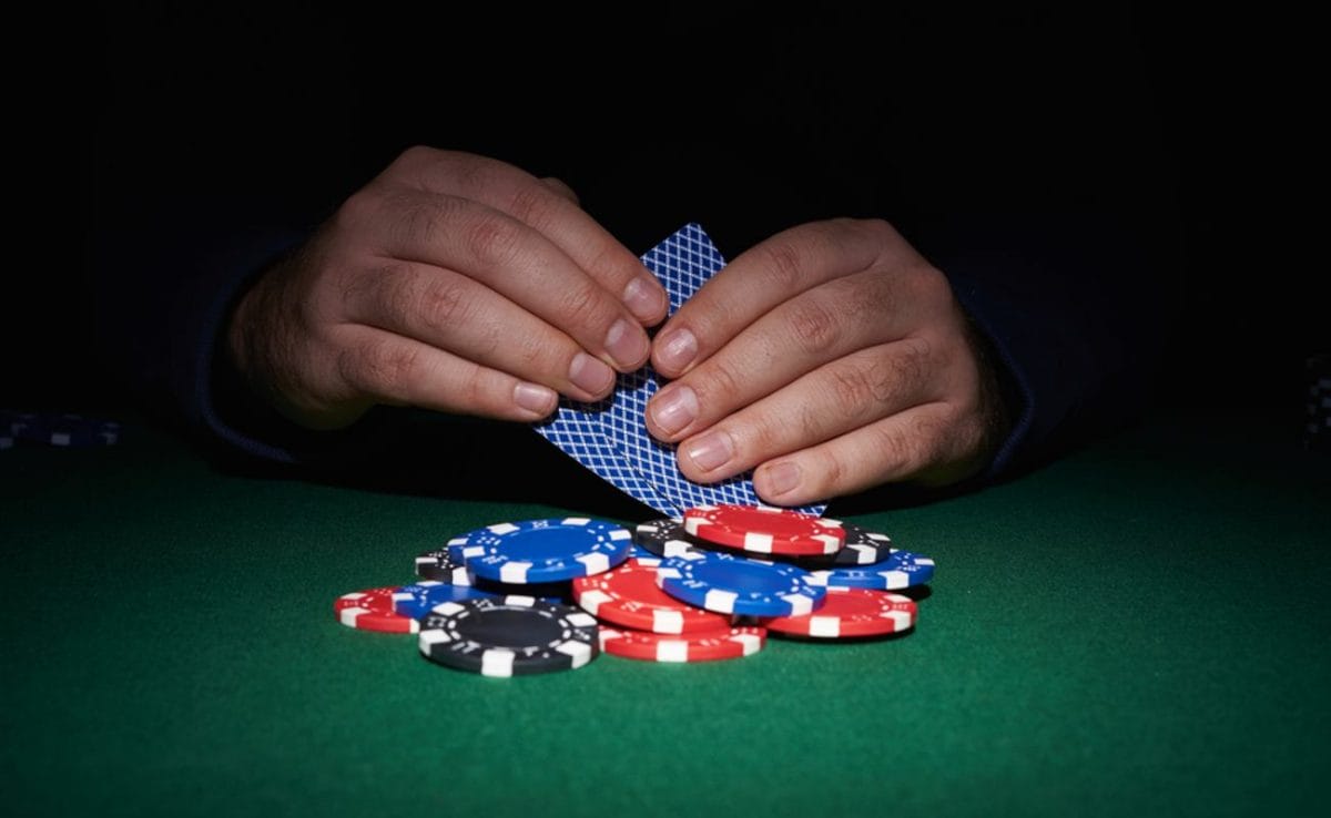 A poker player holds a face-down hand behind some casino chips.