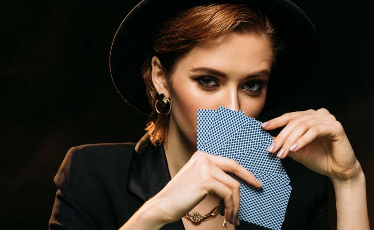 A woman wearing a hat holds her cards up to her face.