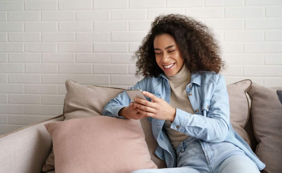 A woman sitting on a couch while playing a game on her smartphone.