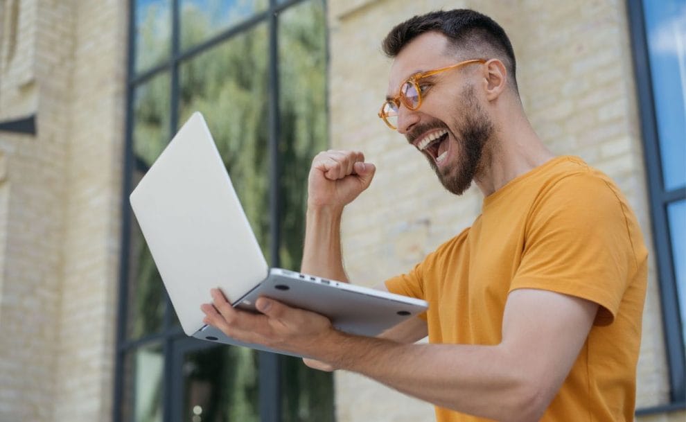 A man celebrating a win while looking excitedly at his laptop screen.