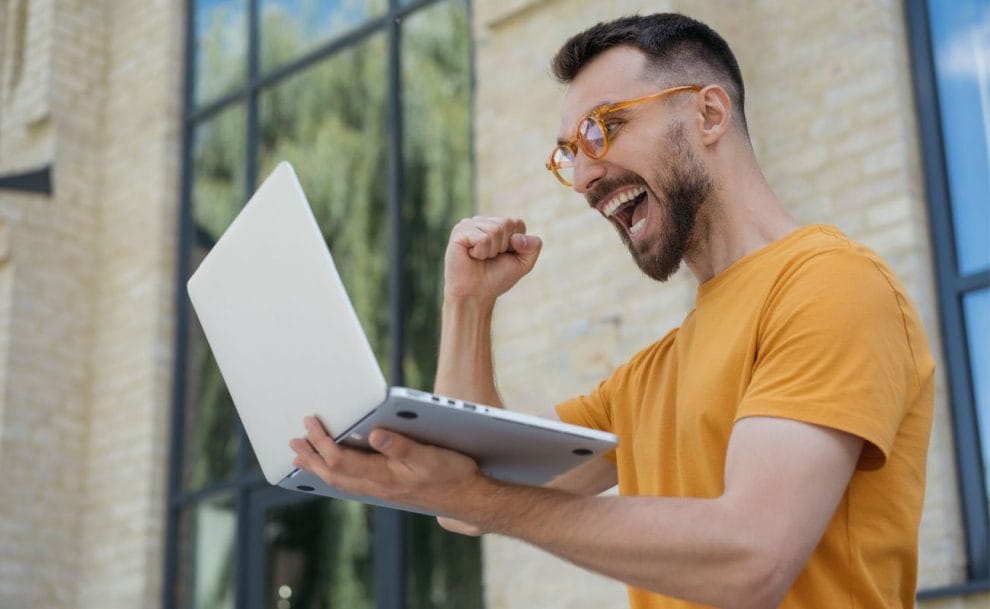  A man celebrating a win while looking excitedly at his laptop screen.