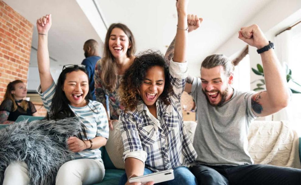 A group of people cheering while looking at a smartphone.