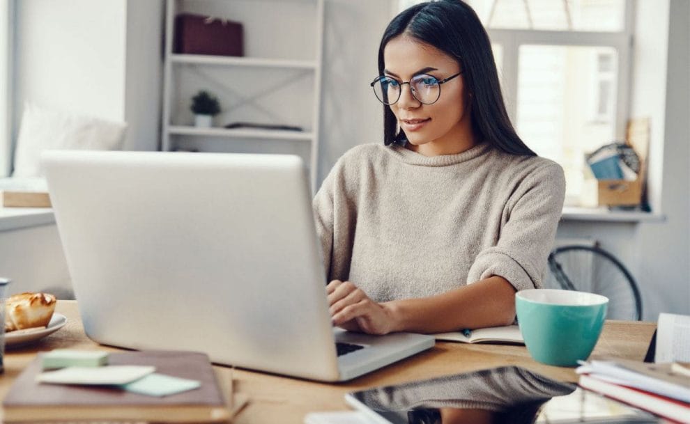 A woman wearing glasses working at her laptop in a casual setting.