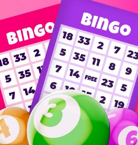 Colorful 3D bingo balls and bingo cards against a pink background.