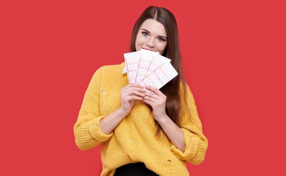 A person wearing a yellow cardigan holding four lottery tickets in front of their face.