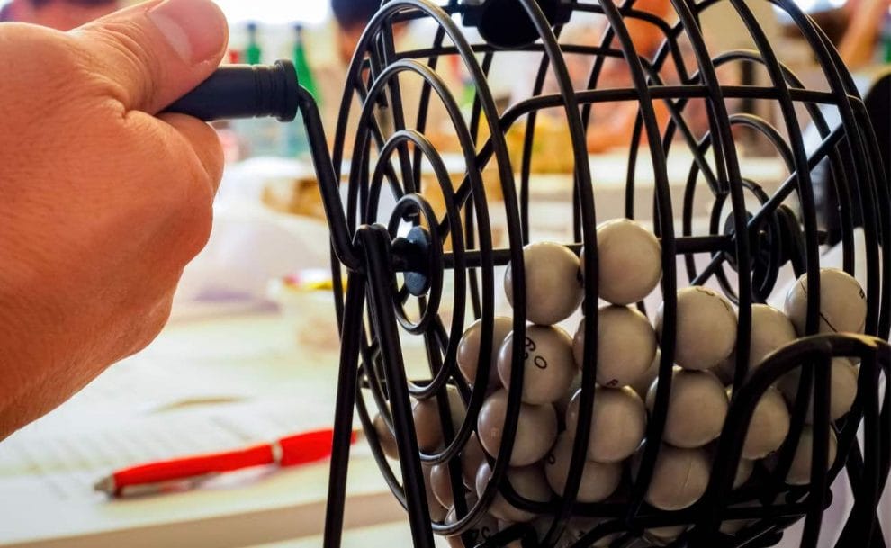 A hand turning a bingo ball cage filled with white bingo balls.