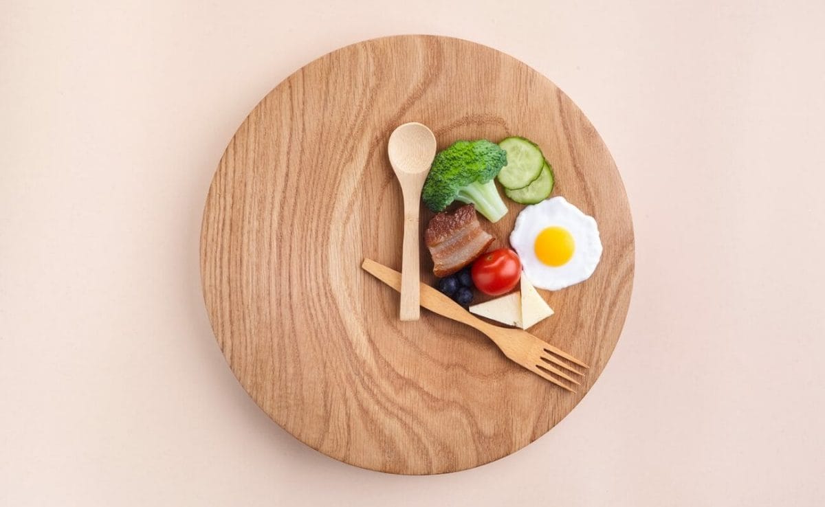 A plate with a fork and spoon arranged to look like a clock, with a portion of food between the fork and the spoon.
