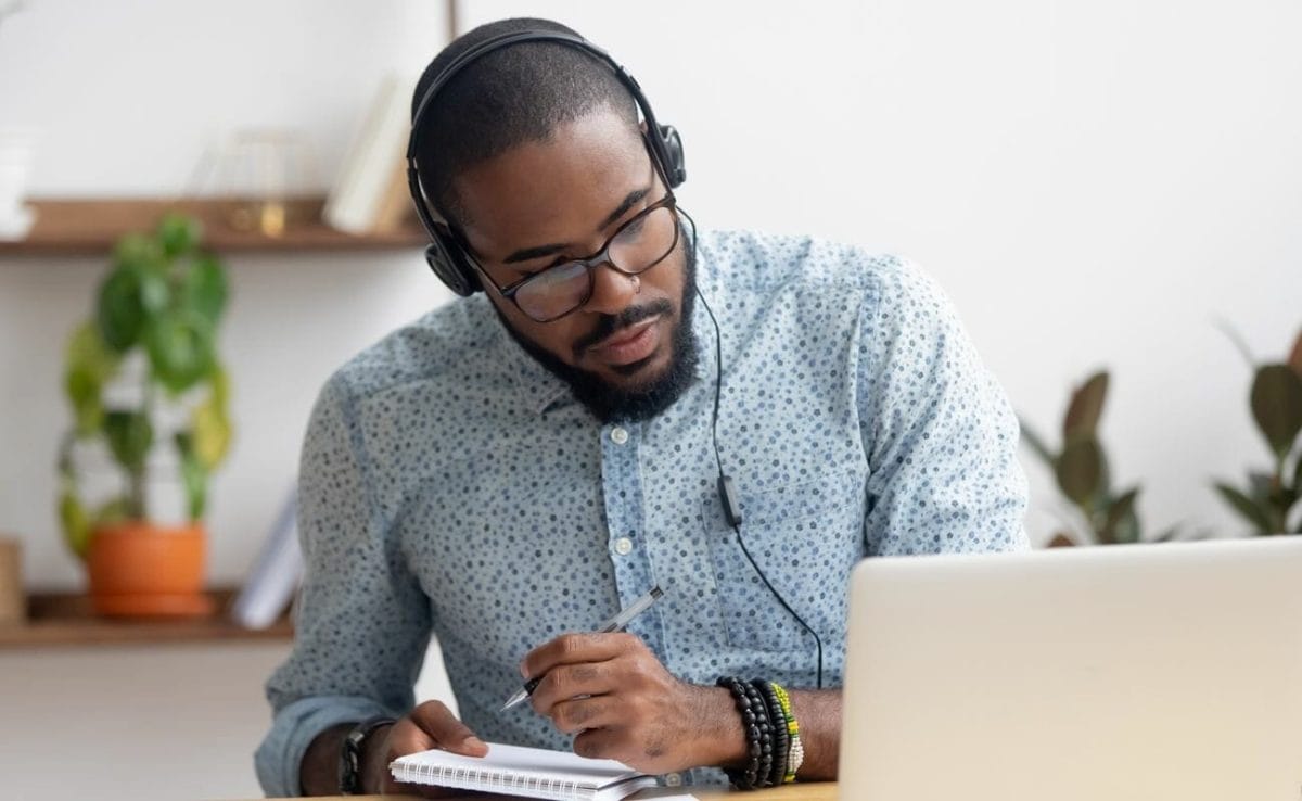 A man wearing headphones sits with a notepad, ready to take notes.