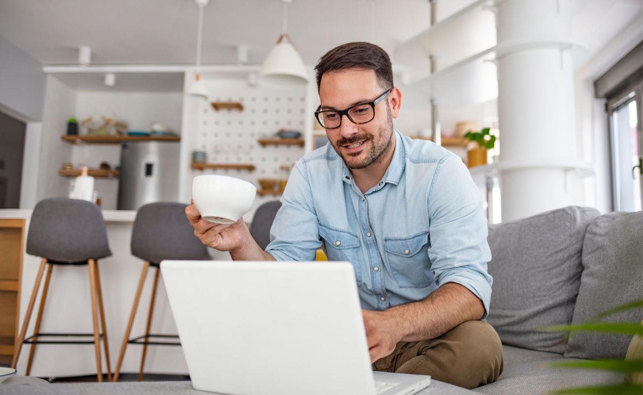 A person drinking a cup of coffee while typing on their laptop.